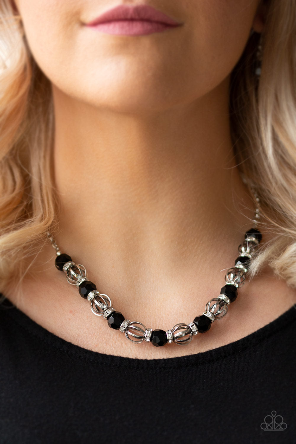 Metro Majestic - Black Necklace - Paparazzi Accessories A collection of airy silver beads, glittery black rhinestone beads, and white rhinestone encrusted rings are threaded along an invisible wire below the collar for a statement-making fashion. Features an adjustable clasp closure.  Sold as one individual necklace. Includes one pair of matching earrings.