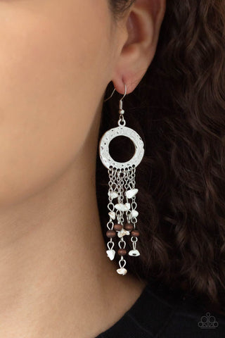 Primal Prestige - White Earrings - Paparazzi Accessories Tapered tassels of dainty wooden beads and white pebbles stream from the bottom of a hammered silver hoop, creating an earthy fringe. Earring attaches to a standard fishhook fitting.  Sold as one pair of earrings.  New Kit