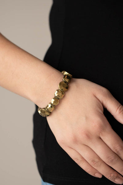 Extra Exposure - Brass Bracelet - Paparazzi Accessories Encased in sleek brass frames, a smoldering collection of round and emerald cut aurum rhinestones glide along stretchy bands around the wrist, creating a sparkly industrial statement piece.  Sold as one individual bracelet.  New Kit