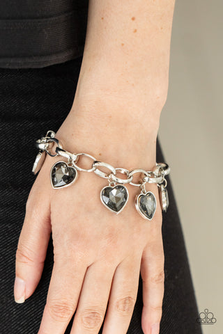 Candy Heart Charmer - Silver Bracelet - Paparazzi Accessories Smoky heart-shaped gems are encased in sleek silver frames that swing from an oversized silver chain, creating a sparkly fringe around the wrist. Features an adjustable clasp closure.  Sold as one individual bracelet.  New Kit