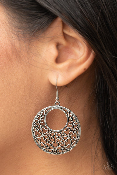 Vineyard Romance - Silver Earrings - Paparazzi Accessories Brushed in an antiqued shimmer, vine-like filigree silver climbs the inside of a studded circular frame, creating a whimsical centerpiece. Earring attaches to a standard fishhook fitting.  Sold as one pair of earrings.  New Kit