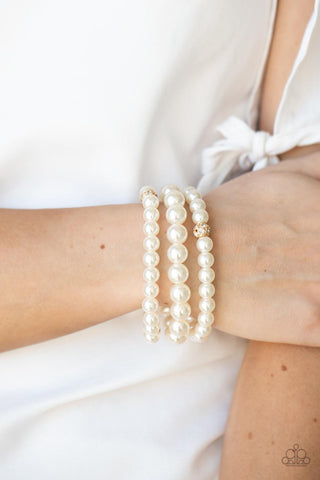 Here Comes The Heiress - Gold Bracelet - Paparazzi Accessories Infused with white rhinestone encrusted gold beads, a bubbly collection of mismatched white pearls are threaded along stretchy bands around the wrist for a vintage inspired layered look.  Sold as one set of three bracelets.  New Kit