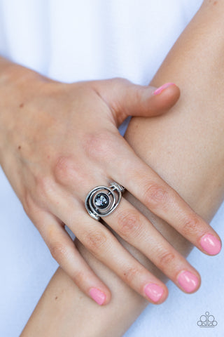 Celestial Karma - Black Ring - Paparazzi Accessories Glistening silver bars swirl around a glassy black bead flecked in iridescent shell, creating an ethereal centerpiece atop the finger. Features a dainty stretchy band atop the finger.  Sold as one individual ring.  New Kit