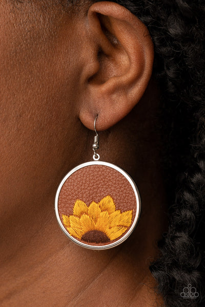 Sun-Kissed Sunflowers - Brown Earrings - Paparazzi Accessories  A golden yellow and brown threaded sunflower is stitched into the bottom of a brown leather frame that is encased in a sleek silver frame, resulting in a whimsical floral fashion. Earring attaches to a standard fishhook fitting.  Sold as one pair of earrings.  New Kit