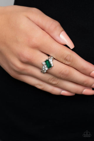 Tip the Balance - Green Ring - Paparazzi Accessories An emerald cut green rhinestone slants across the front of an asymmetrical silver frame dotted in glassy white rhinestones, resulting in a radiant centerpiece atop the finger. Features a stretchy band for a flexible fit.  Sold as one individual ring.